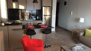 Una cocina moderna con electrodomésticos de acero inoxidable, una zona de comedor con una mesa preparada para cuatro personas y una silla roja.
