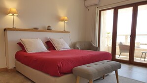 Un dormitorio con cama, dos lámparas de noche, una silla y vistas a través de un ventanal corredero.