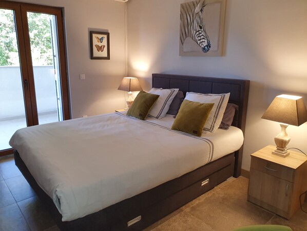 A bedroom with a large bed, two bedside lamps, a nightstand, and a framed butterfly and zebra artwork on the wall. - Luxury apartment with sea view 10 mn from the beach (Donja Lastva)