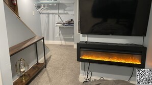 Una sala de estar con un televisor de pantalla plana montado en la pared, una chimenea empotrada y un estante con ropa.