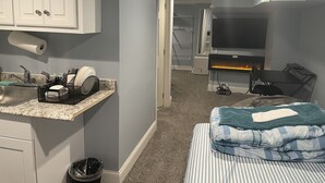 Habitación de hotel compacta con kitchenette, cama con ropa de cama a rayas, televisión y chimenea.