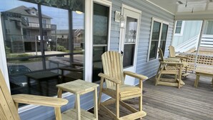 Terraza de madera con sillas Adirondack y una mesa, con vistas a una zona residencial.