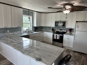A modern kitchen with white cabinets, a granite countertop, a built-in oven, and a microwave. - Cute Beach cottage only minutes from the beach! (Kill Devil Hills)