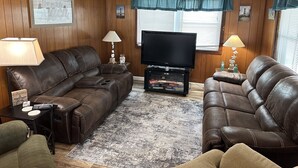 Una sala de estar con dos sofás de cuero marrón, un televisor de pantalla plana y un revestimiento de pared de madera.
