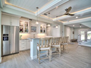 A modern kitchen with a central island, wooden chairs, and a ceiling fan. - Luxury 5 Bedroom Coastal Retreat (Fort Myers Beach)