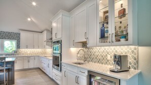 Una cocina moderna con armarios blancos, horno empotrado, máquina de café y refrigerador para bebidas.