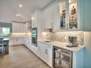 A modern kitchen with white cabinets, a built-in oven, a coffee machine, and a beverage refrigerator. - Luxury 5 Bedroom Coastal Retreat (Fort Myers Beach)