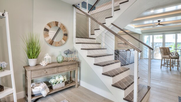 Una escalera moderna con escalones de madera y barandillas de vidrio, que conduce a una sala de estar con un sofá y una mesa de centro.