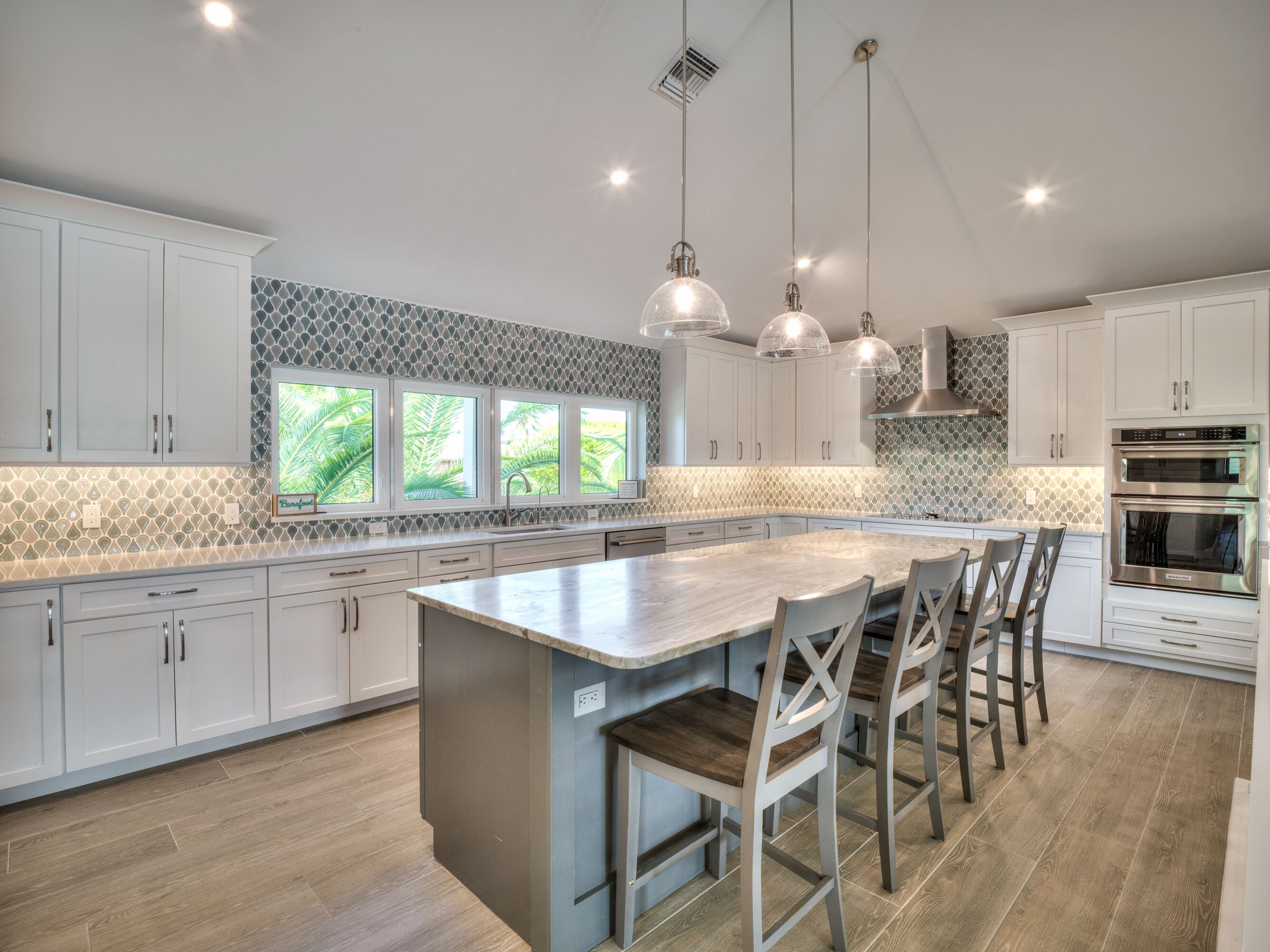 A modern kitchen with white cabinets, a large island, and built-in ovens.