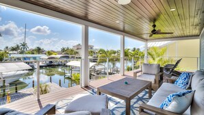 Un espacio al aire libre cubierto con terraza de madera, mobiliario y vista a un puerto deportivo con barcos.