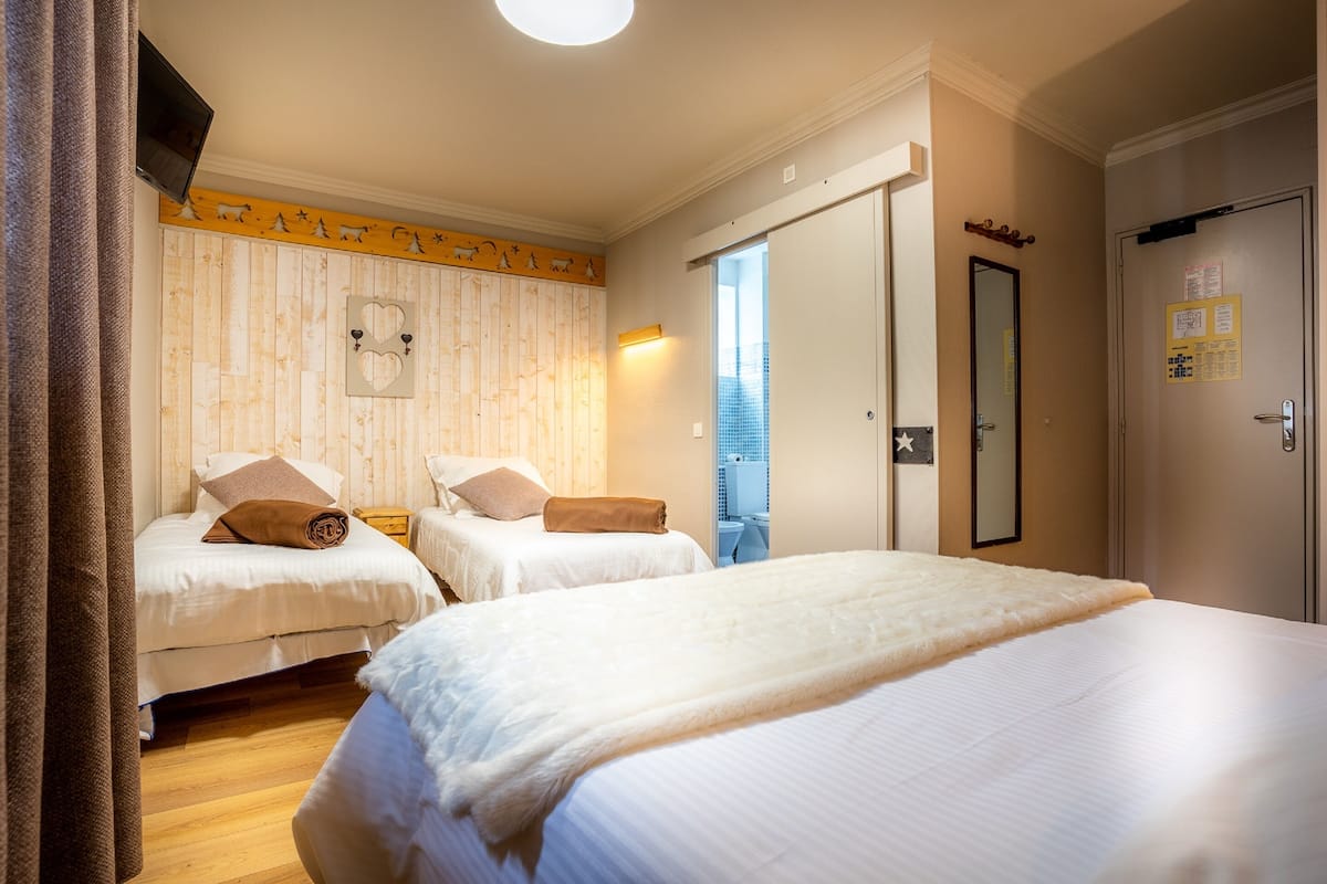 A hotel room with two beds, a wooden wall panel, a ceiling light, and a door with a mirror and a calendar.