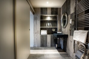 A modern bathroom with a dark wood vanity, a round mirror, and a towel rack.