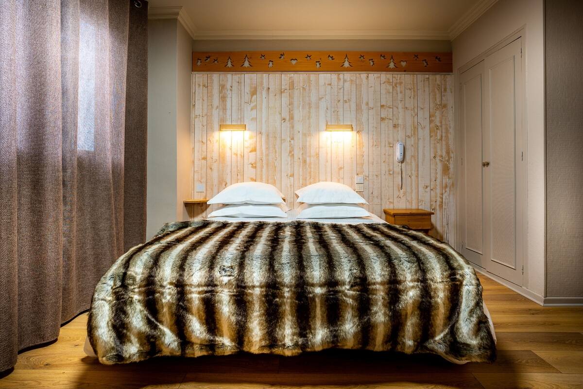 A bedroom with a wooden panel wall, two bedside lamps, a bed with a striped blanket, and a wooden floor.