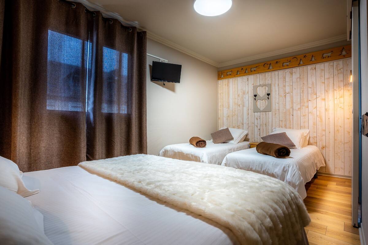 A hotel room with two single beds, a large bed, a flat-screen TV, and a wooden wall with a heart-shaped cutout.