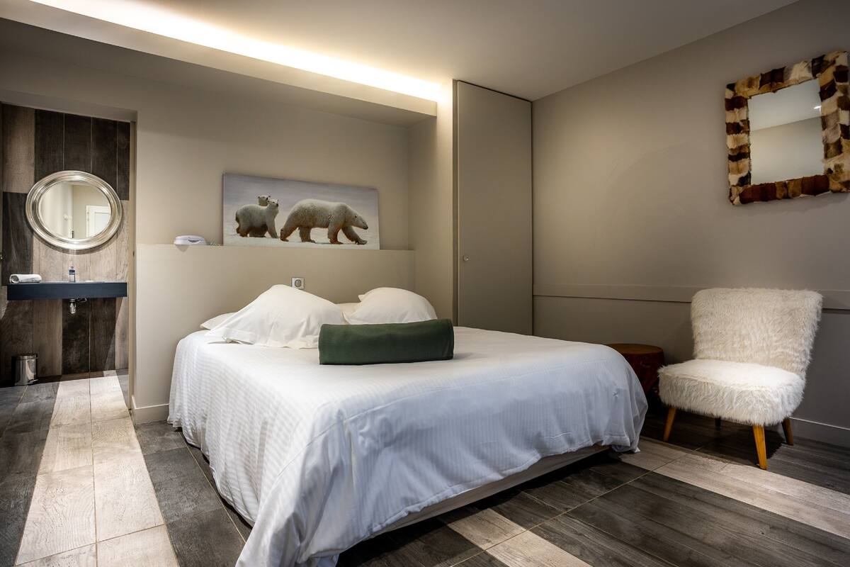 A modern bedroom with a large bed, a round mirror, a fluffy chair, and a polar bear painting on the wall.