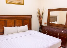 A neatly made bed with white linens, a wooden headboard, a dresser with multiple drawers, and a mirror above it.