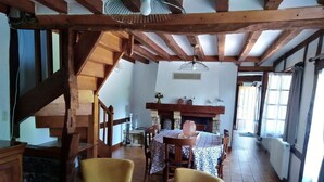 A rustic dining area with wooden chairs, a table with a patterned tablecloth, and a stone fireplace. - Le Clos du Savourey, charming Normandy farmhouse, sleeps 6 (Saint-Aubin-de-Scellon)