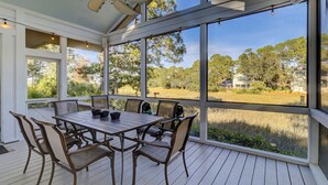 Eine überdachte Terrasse im Freien mit Tisch und Stühlen, große Fenster mit Blick auf ein bewaldetes Gebiet und ein Haus.