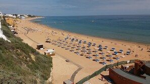 Een strand met rijen ligbedden en parasols, een zandstrand en een heldere blauwe zee.