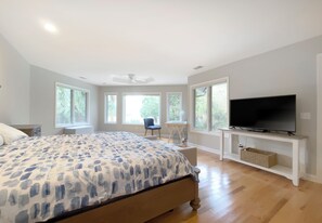 Un dormitorio con una cama grande, un televisor en un mueble bajo, un escritorio y varios ventanales.