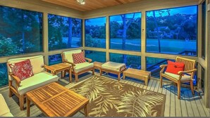 A sunroom with large windows, wooden furniture, and a ceiling fan.