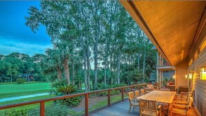 A wooden deck with a table and chairs, overlooking a lush green landscape with trees and a clear sky.