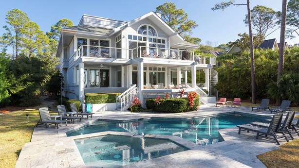 A two-story house with a large pool and outdoor seating.