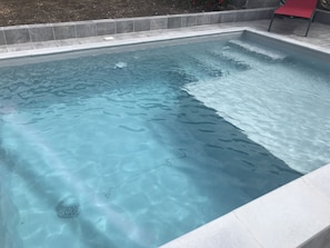 Une piscine rectangulaire à l’eau d’un bleu limpide, bordée de carreaux et entourée d’une bordure en pierre.