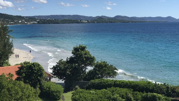 Une vue sur la côte, avec une plage, un ciel dégagé et des montagnes à l’horizon.