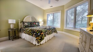 Ein Schlafzimmer mit einem Bett, Nachttischen, einem Schminktisch und großen Fenstern.