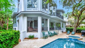 Ein zweistöckiges Haus mit überdachter Terrasse, Sitzgelegenheit im Freien und einem Schwimmbecken.