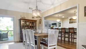 Un coin repas avec une table en bois et des chaises blanches, un lustre et un buffet aux portes vitrées.