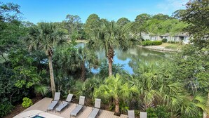 Un espace piscine avec des chaises longues et une vue sur un lac entouré d’arbres.