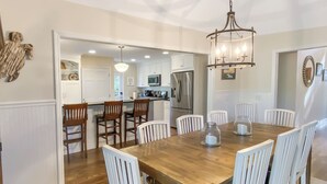 Une cuisine spacieuse avec des meubles blancs, une table à manger en bois et des chaises blanches.