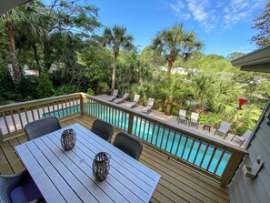 A wooden deck with a pool, lounge chairs, and a table with decorative items. - 21 Wren Drive at The Sea Pines Resort (Hilton Head Island)