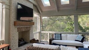 A sunroom with a stone fireplace, a flat-screen TV, and a ceiling fan. - 23 Oyster Landing Road at The Sea Pines Resort (Hilton Head Island)