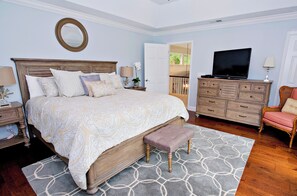 Un dormitorio con una cama grande, cabecera de madera, televisión, cómoda y una silla.