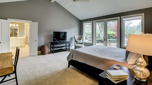 Een slaapkamer met een groot bed, een televisie, een stoel en een bureau met boeken en een lamp.