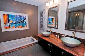 Een moderne badkamer met een bad, twee wastafels met ronde glazen kommen en een grote spiegel.