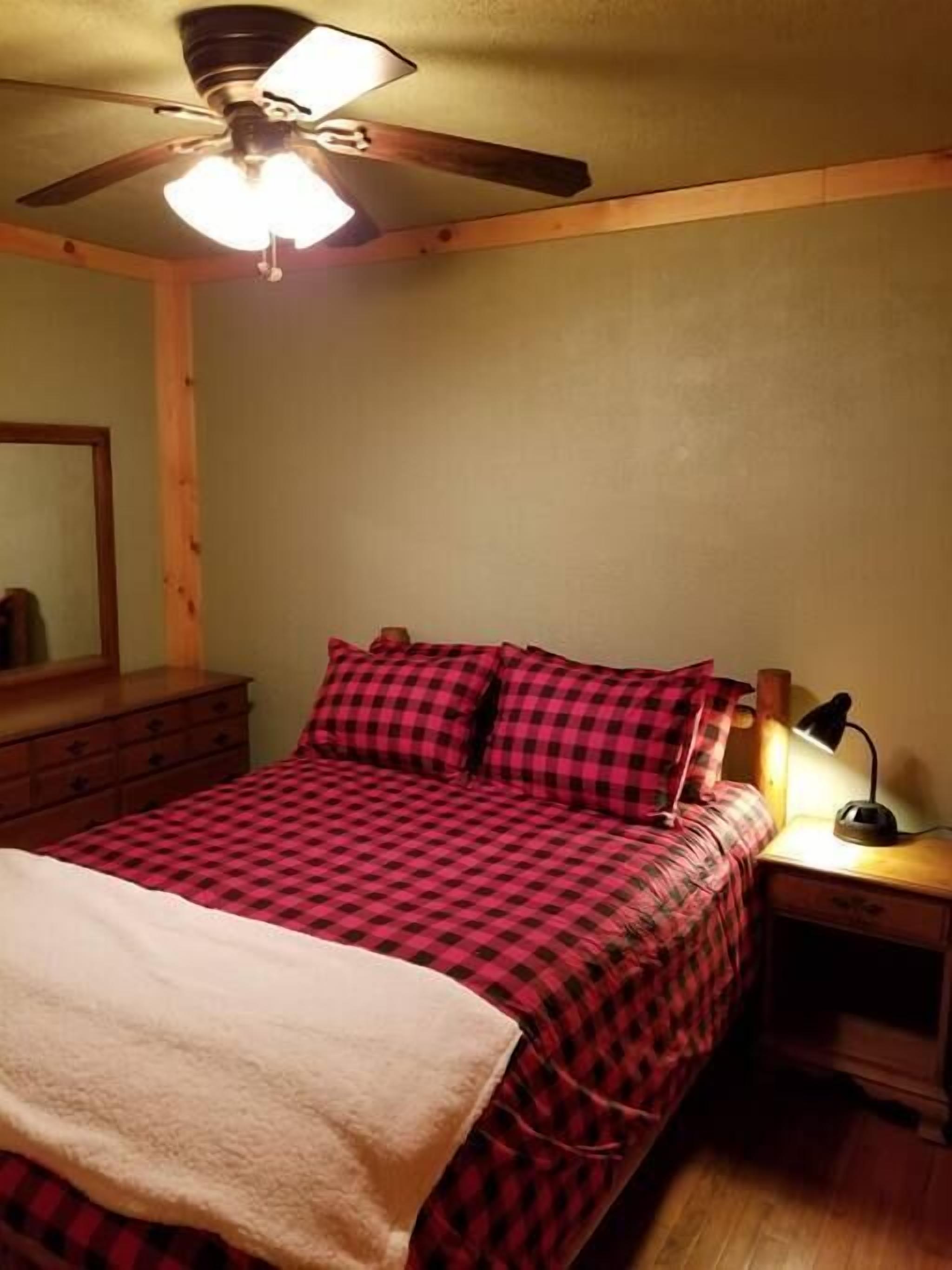 Un dormitorio con cama, mesita de noche, escritorio, ventilador de techo y espejo.