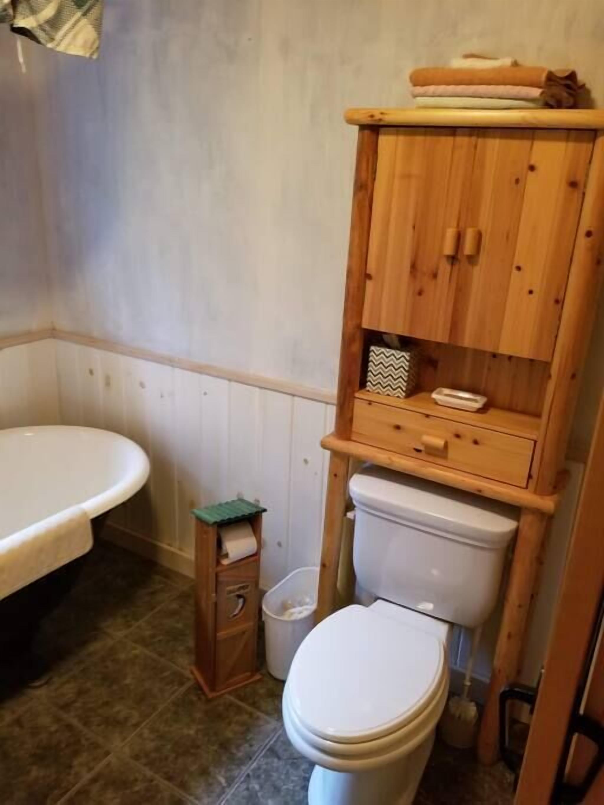 A bathroom with a wooden cabinet, a toilet, and a bathtub.