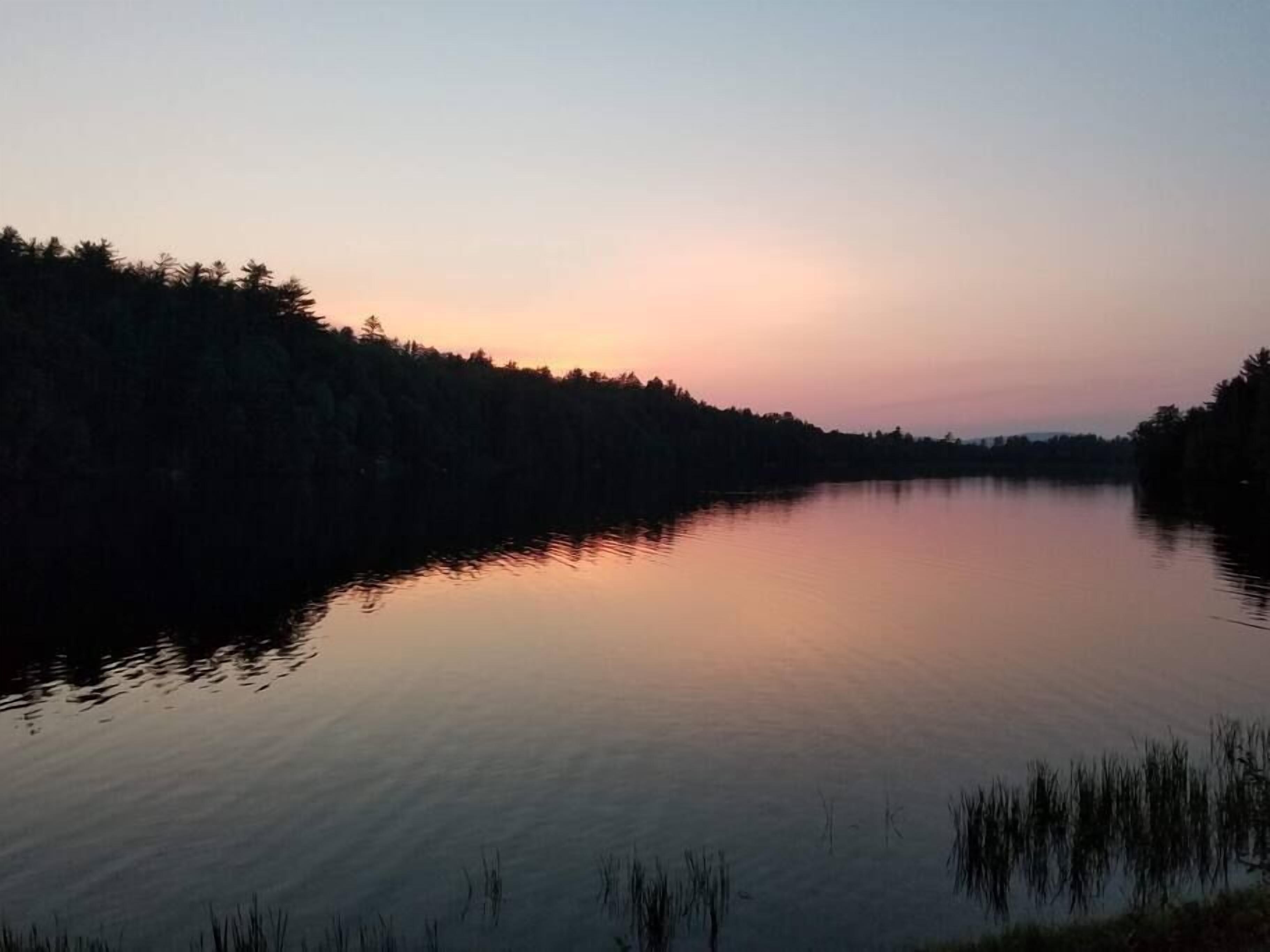 Een rustig meer bij zonsondergang met een bebost oever.