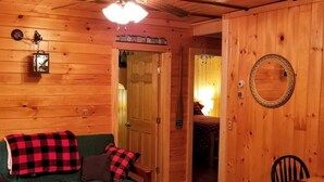 Interior acogedor de una cabaña con piso de madera, un sofá verde con mantas a cuadros, una mesa de comedor con sillas y un espejo en la pared.