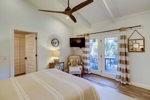 Une chambre avec un lit, un ventilateur de plafond, une télévision, une chaise et une vue sur l’extérieur grâce à une porte coulissante.
