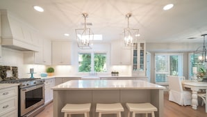 Een moderne keuken met witte kasten, een centraal eiland met barkrukken en hanglampen.