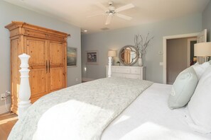 Une chambre avec un grand lit, une armoire en bois et un ventilateur de plafond.