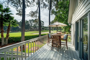 Une terrasse en bois avec une table et des chaises, donnant sur un terrain de golf.
