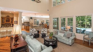 A spacious living area with a kitchen in the background, large windows, and a ceiling fan. - 34 Baynard Cove Rd. at The Sea Pines Resort (Hilton Head Island)