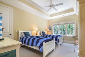 A bedroom with two beds, a ceiling fan, a window with a view of greenery, and a door with a striped towel. - 34 Baynard Cove Rd. at The Sea Pines Resort (Hilton Head Island)