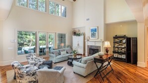 A spacious living room with a high ceiling, large windows, and a fireplace. - 34 Baynard Cove Rd. at The Sea Pines Resort (Hilton Head Island)